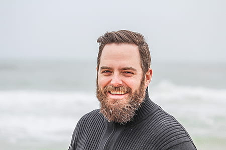 Man Wearing Black Zip-up Jacket Near Beach Smiling at the Photo thumbnail