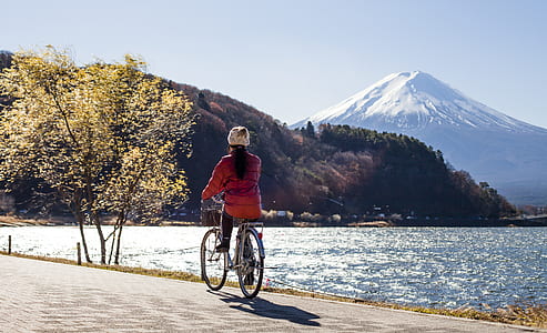 woman riding on bicycle near a body of water with Mount Fuji in background thumbnail