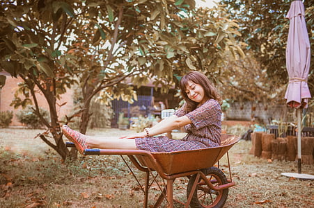 woman sits on brown metal wheelbarrow during daytime thumbnail