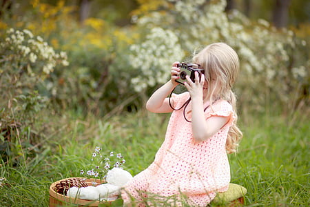 girl sitting on grass field holding black camera thumbnail
