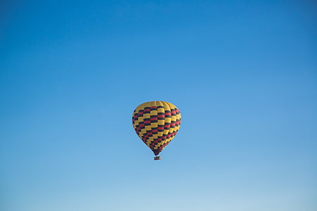 yellow, red, and black hot air balloon flying under blue sky thumbnail