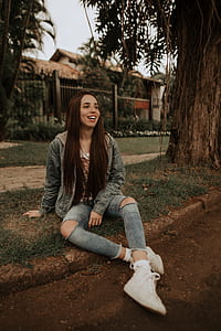 brown haired woman in blue denim jacket sitting on grass near tree thumbnail