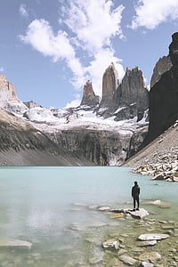 man standing on rock in body of water near mountains thumbnail