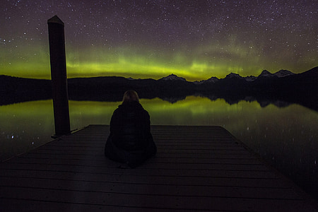 person sitting on dock bridge under Northern Lights thumbnail