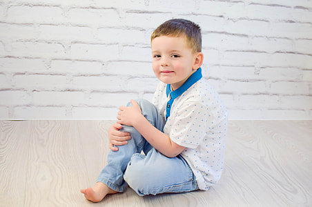 boy in white and blue polka-dots polo shirt and blue jeans sitting on brown wooden floor thumbnail