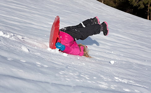 flipped over child riding red plastic sled on snow during daytime thumbnail
