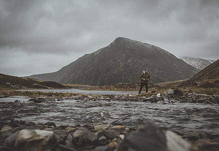 man standing beside body of river with mountain at distance during daytime thumbnail