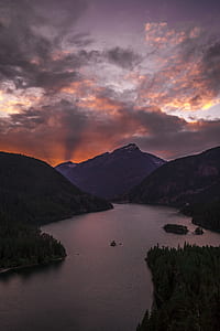 body of water between mountain under white and orange cloudy sky thumbnail
