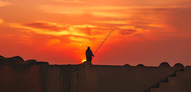 silhouette of person standing while using fishing reel thumbnail
