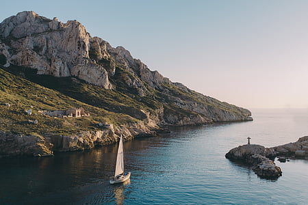 person on rock near white boat and mountain thumbnail