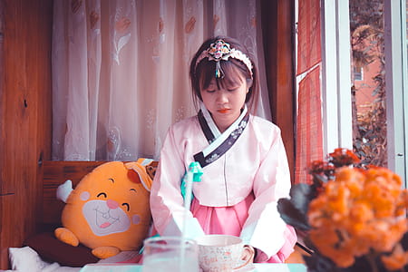 Woman Wearing White and Pink Traditional Korean Dress Sitting Near Yellow Plush Toy thumbnail