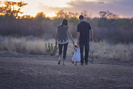 man, woman, and toddler walking near grasses during golden hour thumbnail