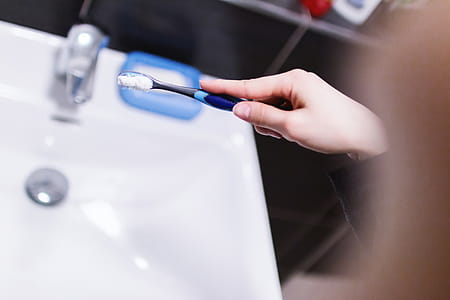 Woman hand holding toothbrush with toothpaste applied on it in bathroom thumbnail