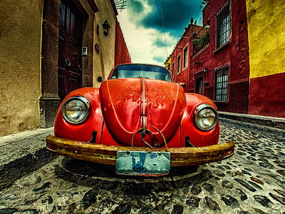 red Volkswagen Beetle coupe parked at the road near buildings thumbnail