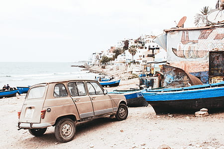 brown 5-door hatchback beside blue and black boat on seashore at daytime thumbnail