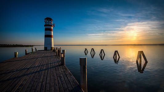 photo of white and red lighthouse near body of water under blue sky thumbnail