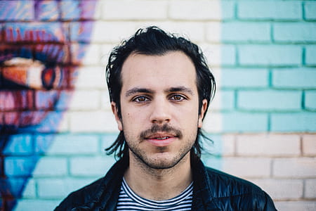 man in black jacket and white and black striped shirt looking straight thumbnail