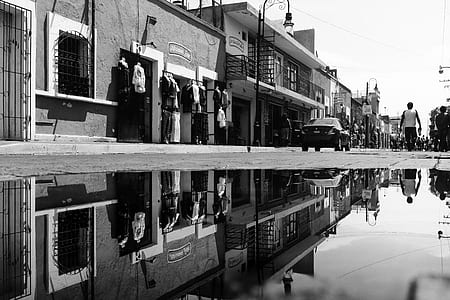 grayscale photography of people near car and houses thumbnail