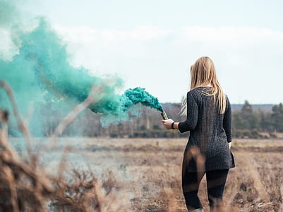 woman holding smoke bomb walking on brown field thumbnail
