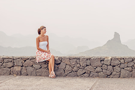 woman in white sleeveless dress sitting in stone bench thumbnail
