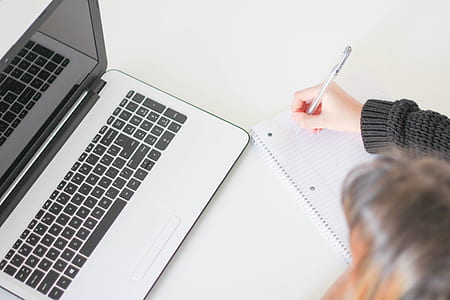 person writing on white lined paper beside laptop thumbnail