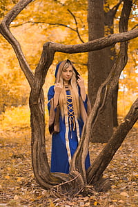 woman wearing blue and gold dress standing beside tree thumbnail