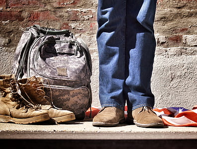 US Army standing beside camouflage bag and pair of brown combat boots thumbnail