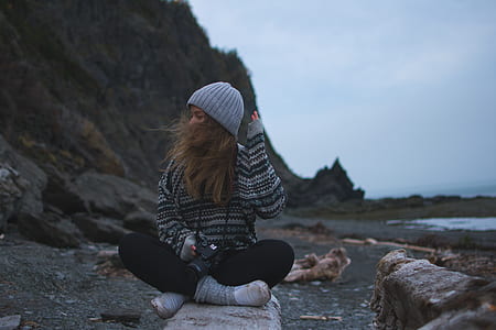 woman in gray and black sweater sitting on rock near body of water thumbnail
