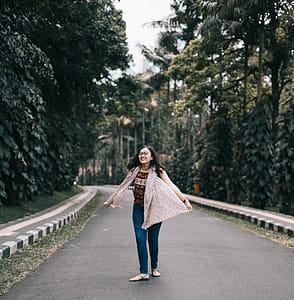 Woman Standing on Road Between Trees thumbnail