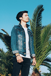 man in blue denim jacket standing near palm tree thumbnail