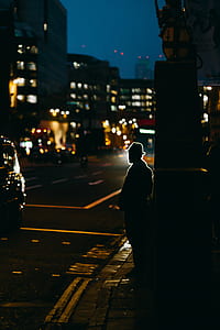 silhouette of man wearing hat standing near road with cars at night thumbnail