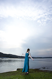 woman wearing teal sleeveless long dress standing on grass field near body of water thumbnail