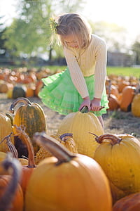 girl in white sweatshirt holding a yellow pumpkin during daytime thumbnail