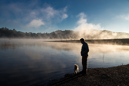 silhouette photography of man and dog standing near lake thumbnail