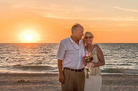man wearing white dress shirt with woman wearing yellow floral tank top standing on shoreline during golden hour thumbnail