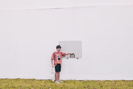 boy standing beside white painted wall outdoor during day thumbnail