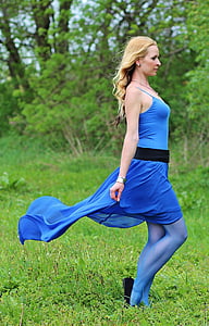 photograph of woman wearing blue spaghetti strap dress standing on grass field making side view posture thumbnail