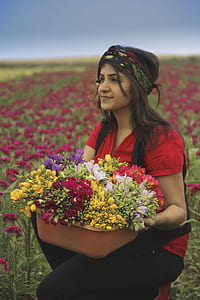 woman holding flowers basket taking photo beside flower field at daytime thumbnail