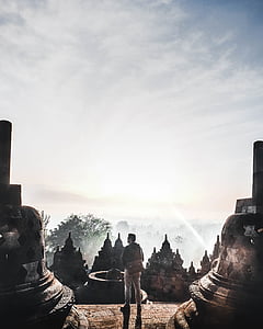 man standing on stair beside statues against light during daytime thumbnail