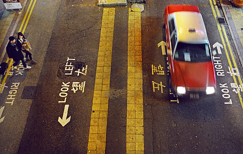speeding red and grey sedan on road with couple nearby crossing street during nighttime thumbnail