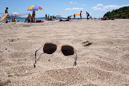 sunglasses on sand beside group of people thumbnail