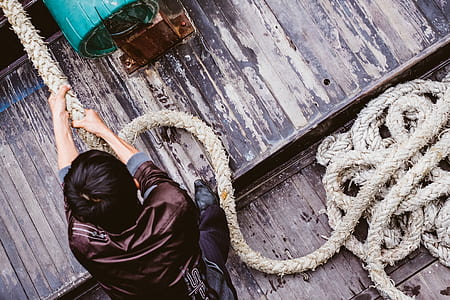 man pulling a gray rope sitting on brown wooden dock thumbnail