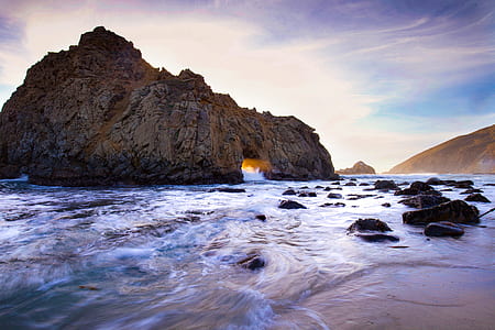 brown rock formation in body of water under cloudy sky thumbnail