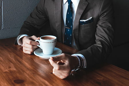 man in suit holding mug with coffee sitting on chair front of table in room thumbnail