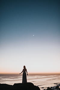 silhouette of woman standing on rock near body of water thumbnail