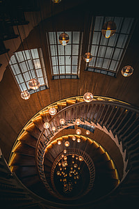 spiral brown wooden stairway with pendant lamps and windows on wall thumbnail
