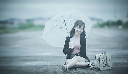 woman holding umbrella while sitting on road during daytime thumbnail