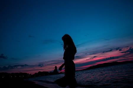 silhouette of woman standing on sandy ground at night time thumbnail