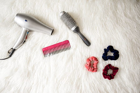 gray hair blower beside two pink and gray hair combs and three hair scrunchies on white fur textile thumbnail