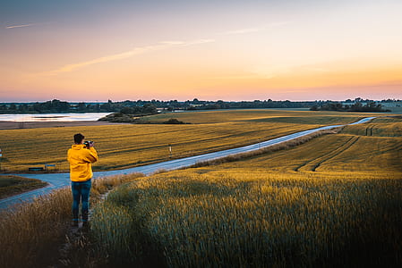 man taking photo of green grass field with body of water during daytime thumbnail